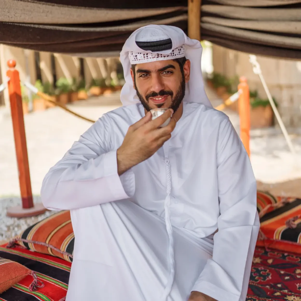 a man sitting on a rug holding a cup