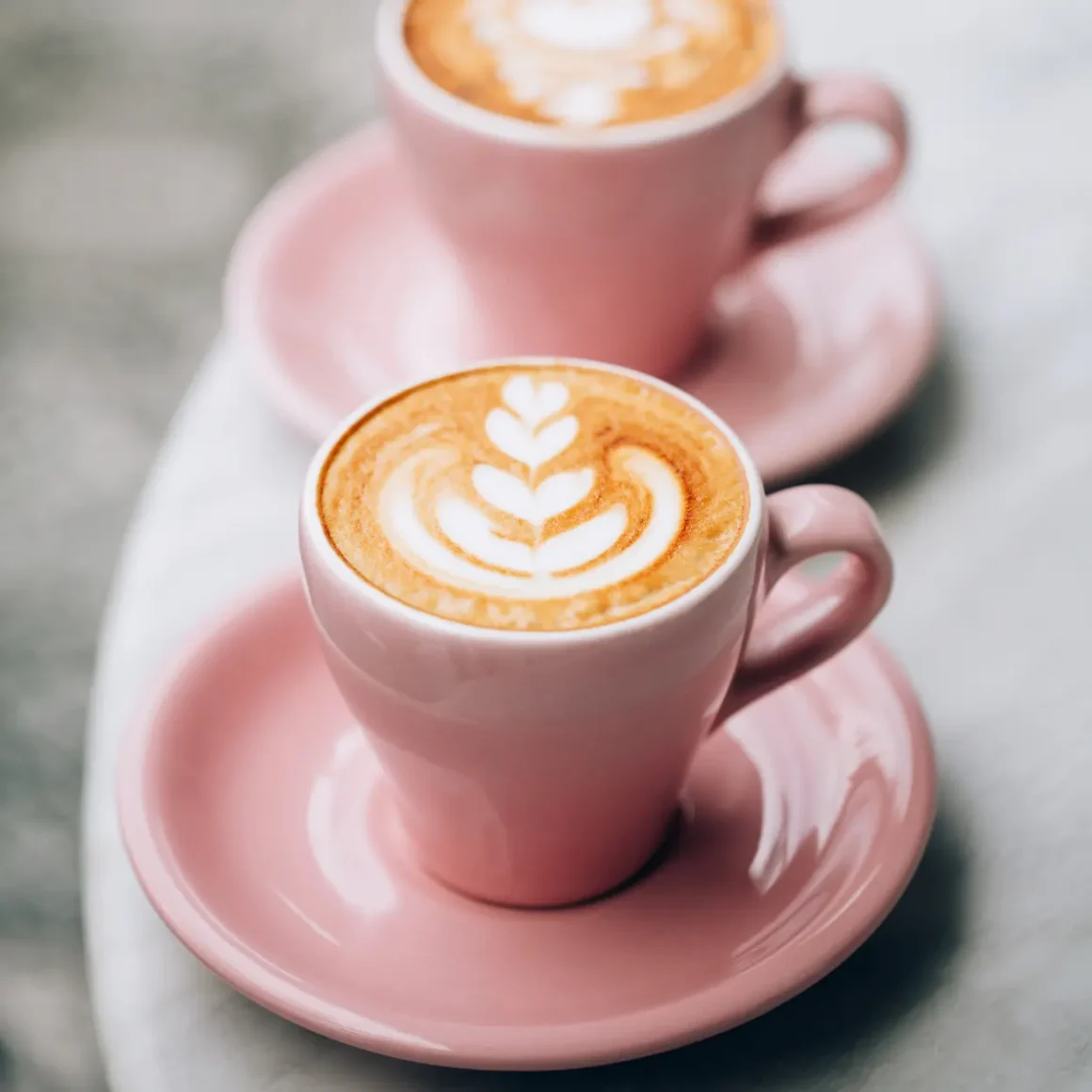 two pink cups of wet cappuccino coffee with a leaf design on top