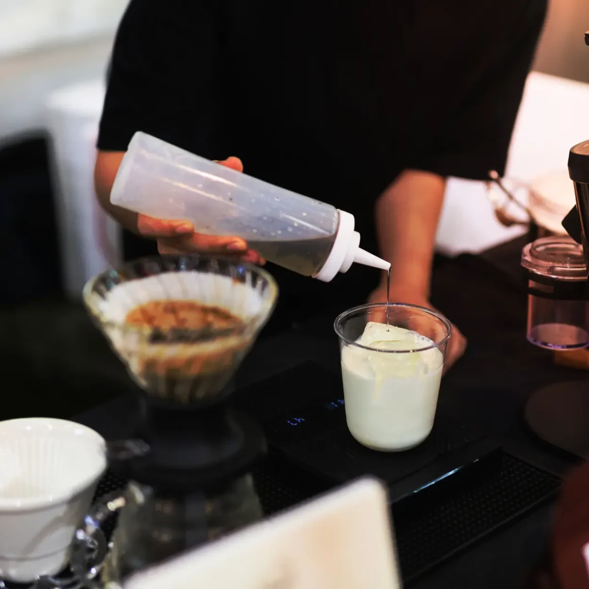 barista adding coffee syrup into a glass of milk