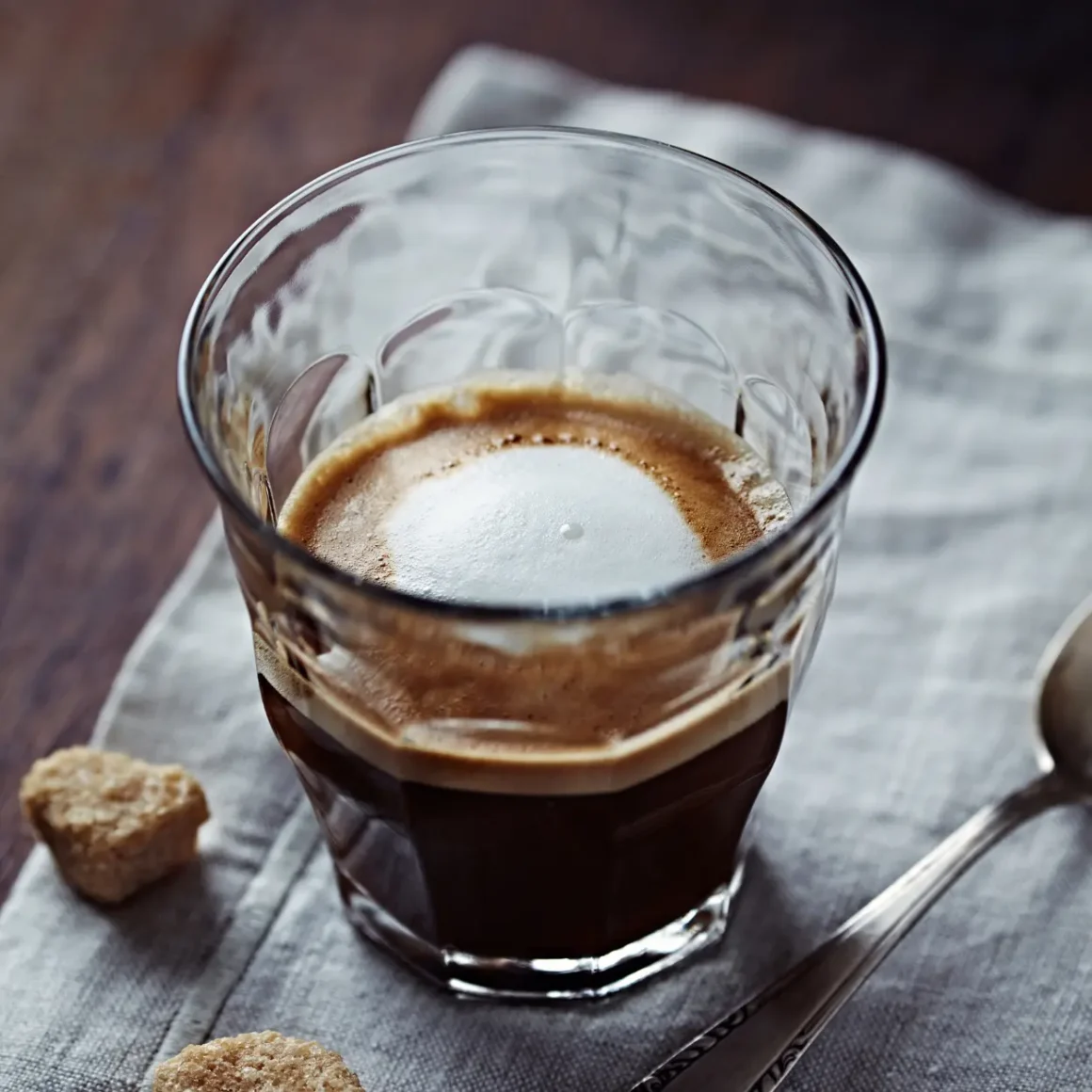 a glass of macchiato coffee with a spoon and sugar cubes