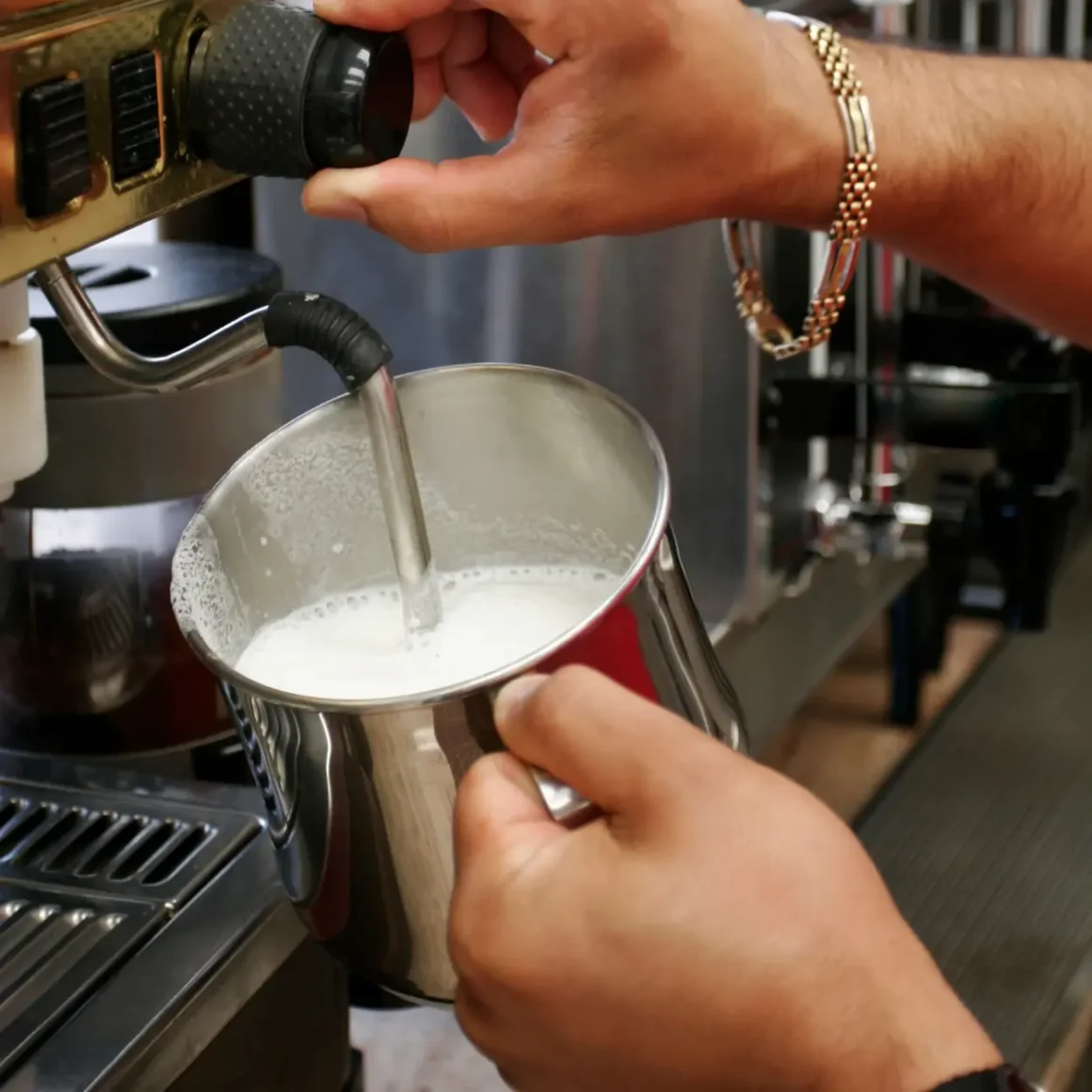 barista pouring milk into a pot from an espresso machine