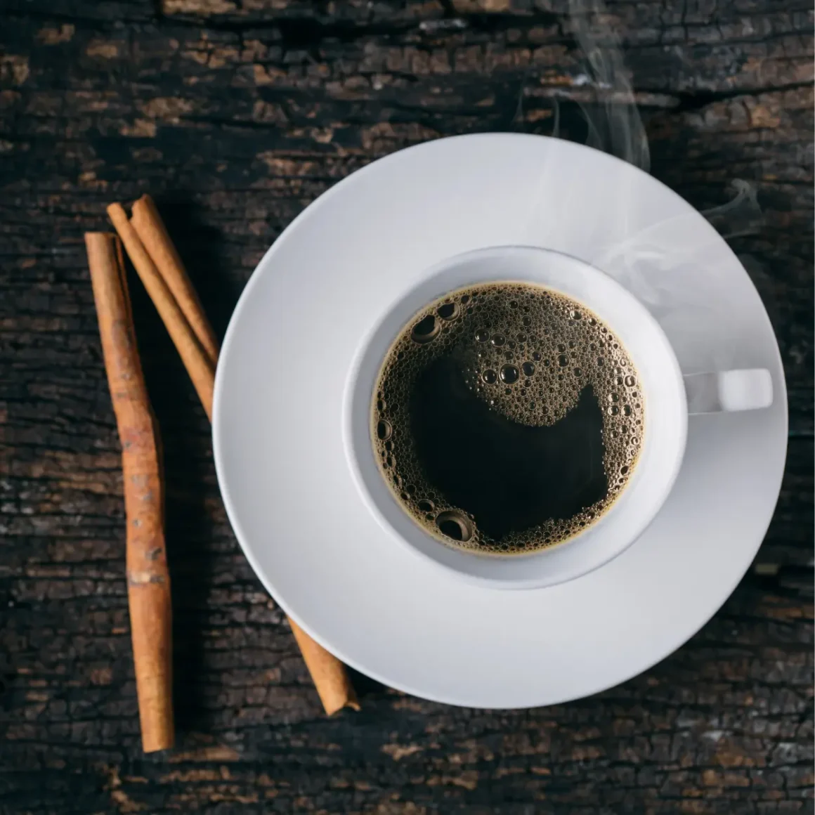 a cup of coffee and cinnamon sticks on a wood surface