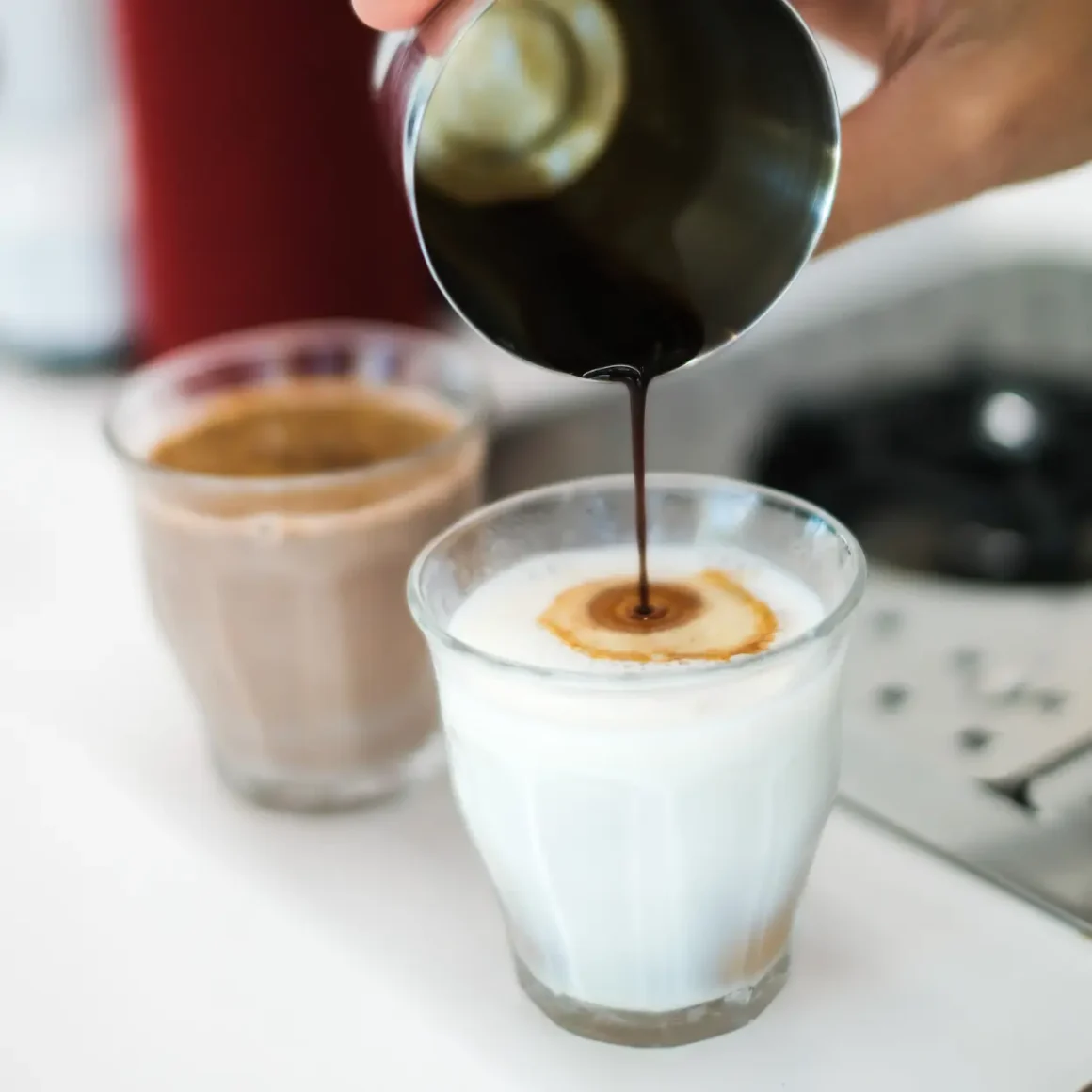 a person pouring a espresso into a glass of milk