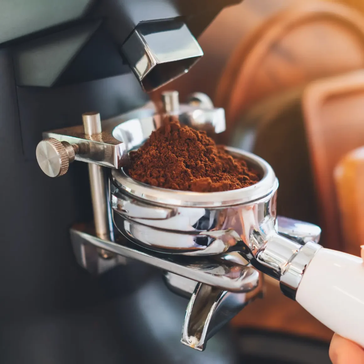 a hand holding a portafilter filled with ground coffee