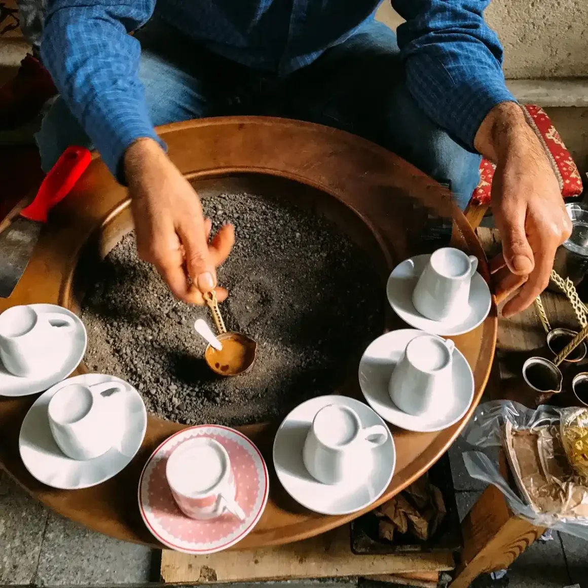 barista brewing turkish coffee with a tray of coffee cups and a spoon