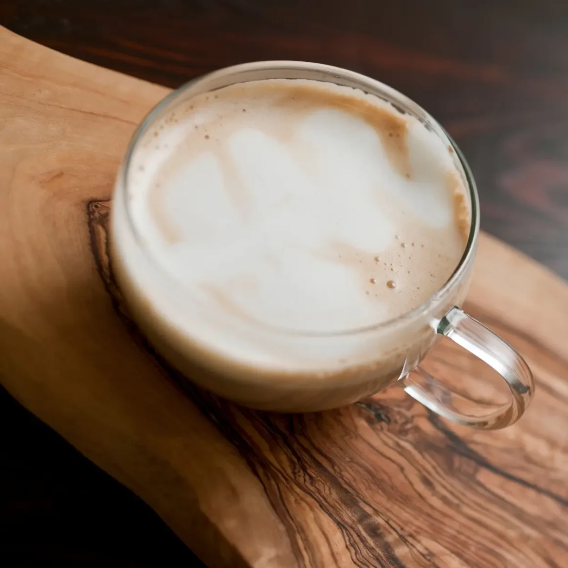 a glass cup of café con leche coffee on a wood surface