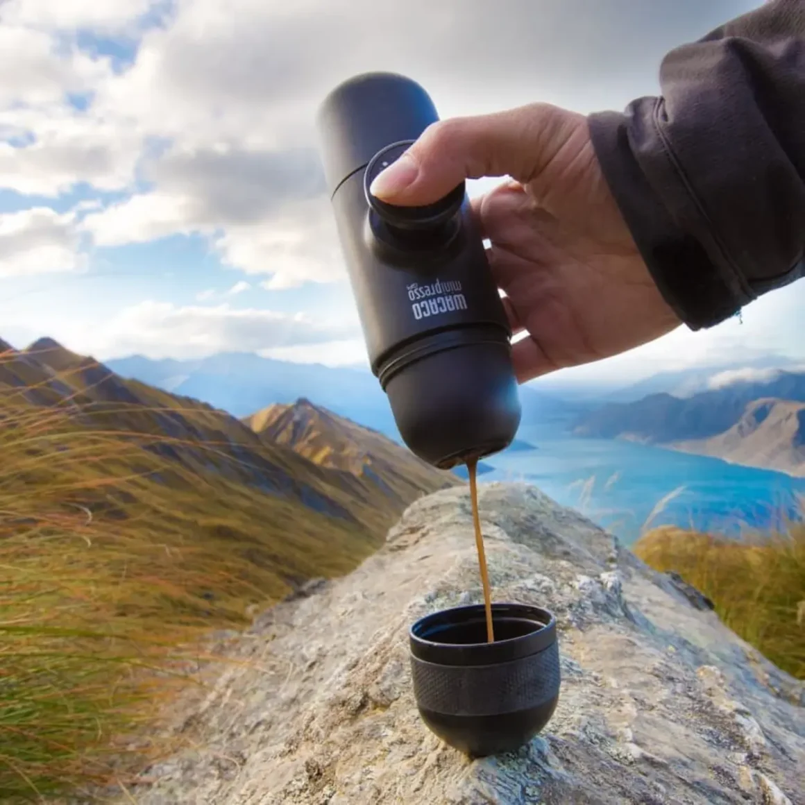 a hand holding a wacaco minipresso gr pouring coffee into a cup