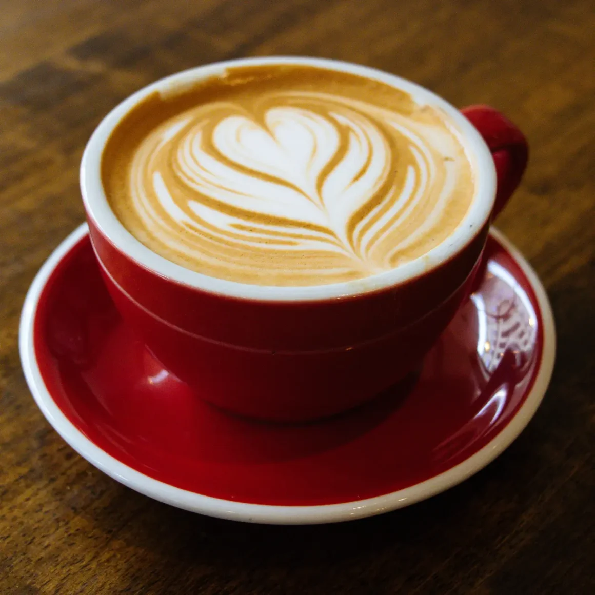 a red cup of cappuccino coffee with a heart shaped foam in it