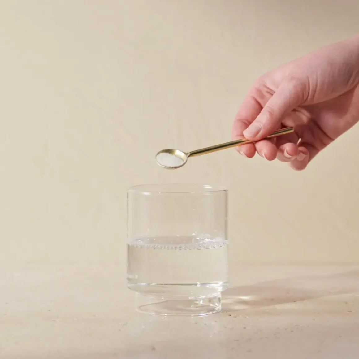 a hand holding a spoon over a glass of water