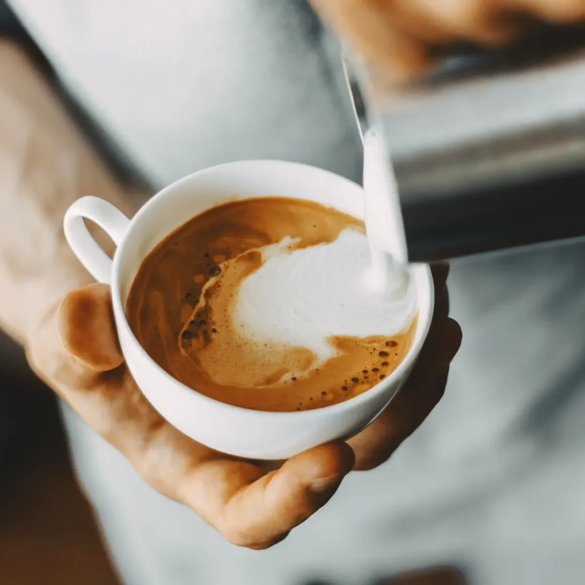 barista pouring milk into a cup of wet cappuccino coffee