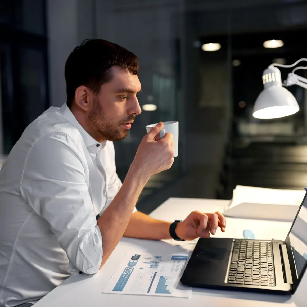 a man sitting at a desk with a laptop and a cup of decaf coffee