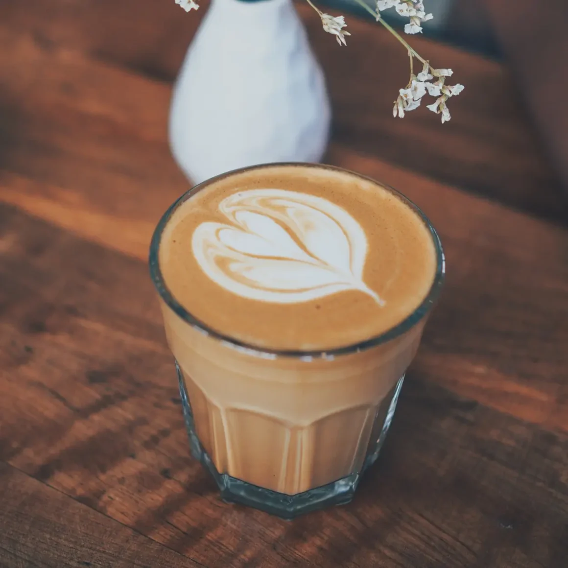 a glass of latte with a flower design in the foam