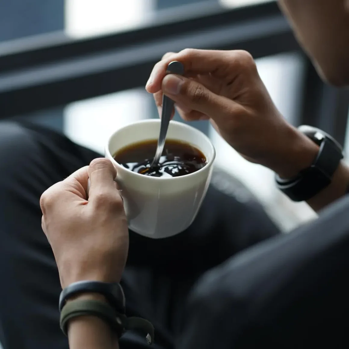 a person holding a cup of coffee and stirring