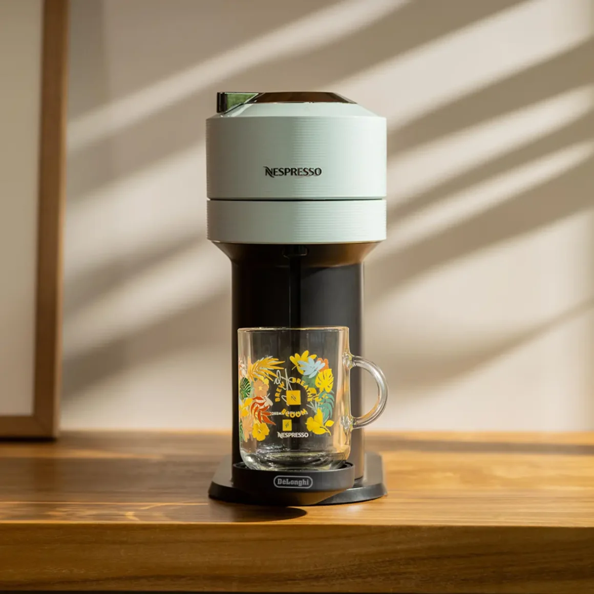 a nespresso vertuo next coffee machine with a glass cup on a table