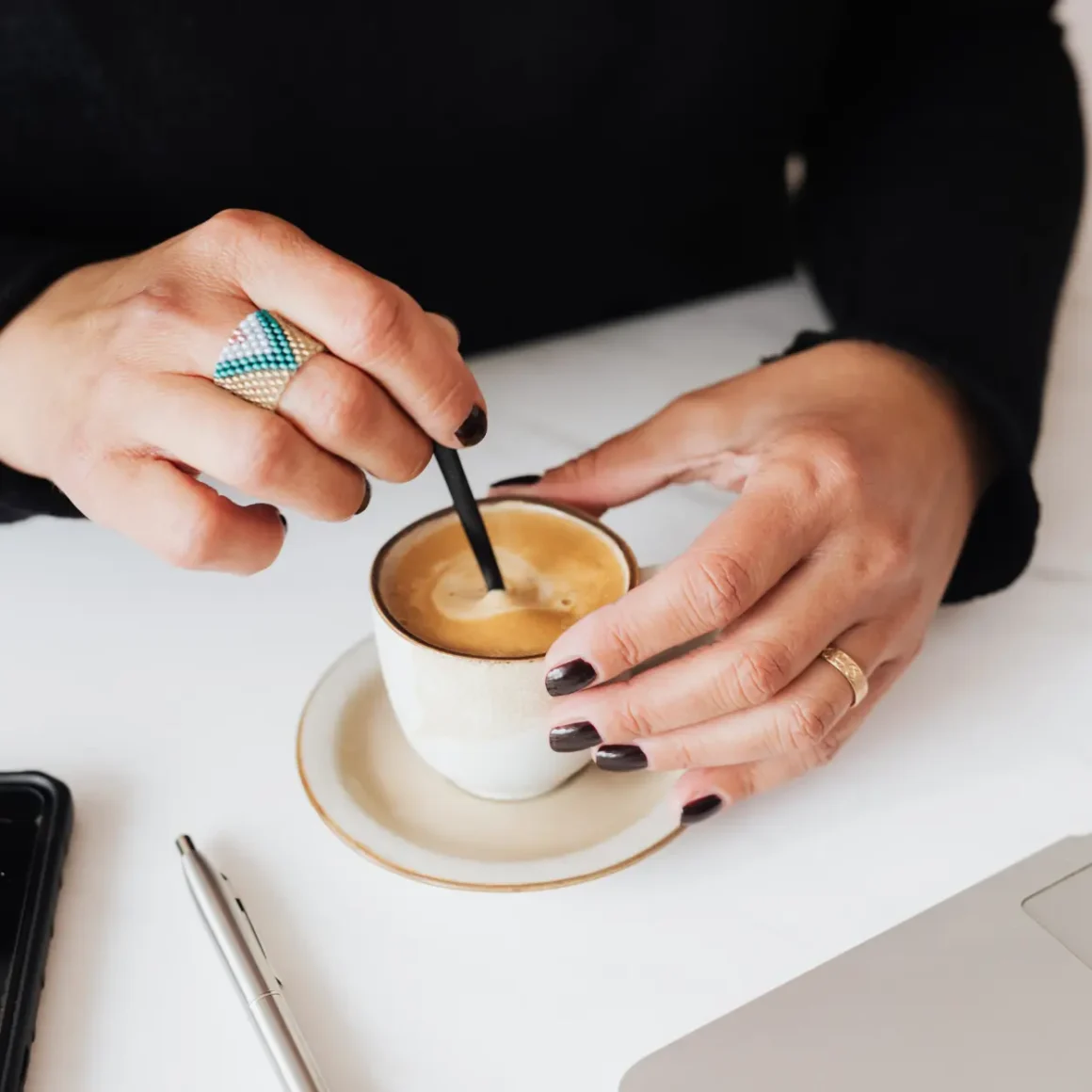 a person's hands holding a spoon in a cup of regular espresso