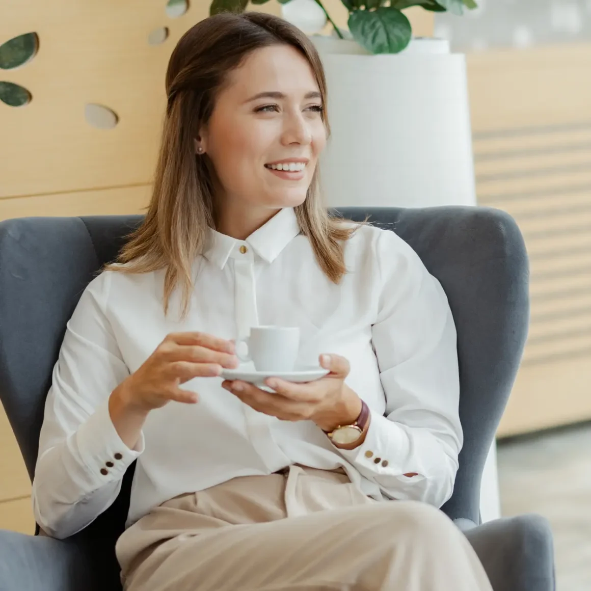 a woman sitting in a chair holding a cup of dead espresso and saucer