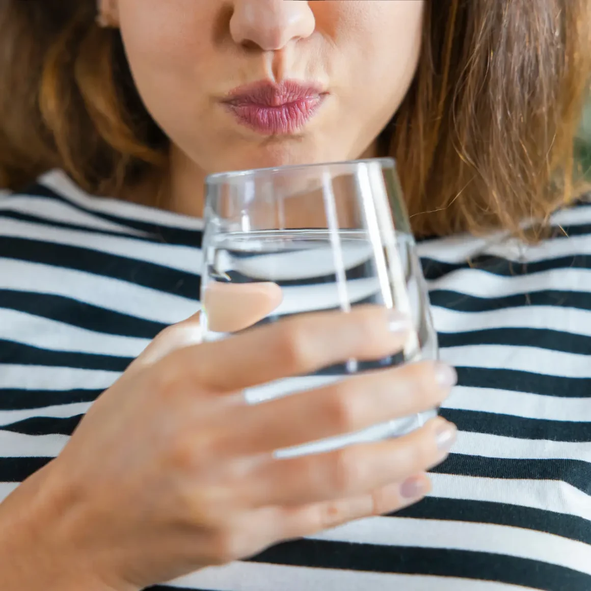 a woman drinking water from a glass for cooling her burnt tongue