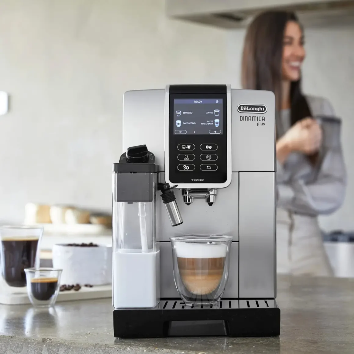 woman standing behind a delonghi dinamica plus coffee maker on a counter