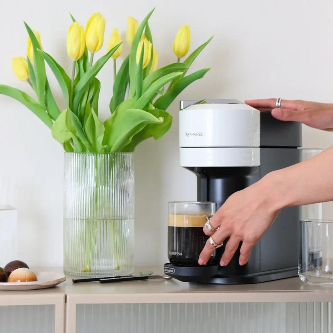 a person pouring a coffee cup into a nespresso vertuo next coffee machine