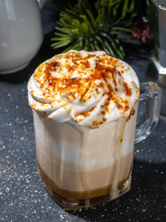 a glass cup of caramel brulee latte christmas coffee drink whipped cream and a sprinkle of orange flakes