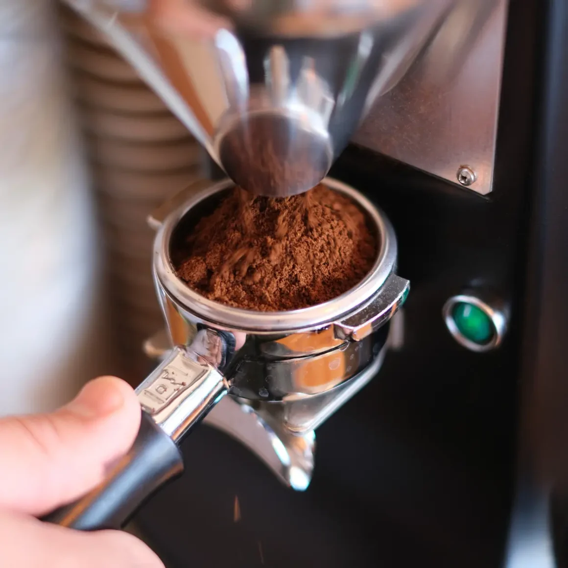 barista holding a portafilter filled with ground coffee and an espresso machine