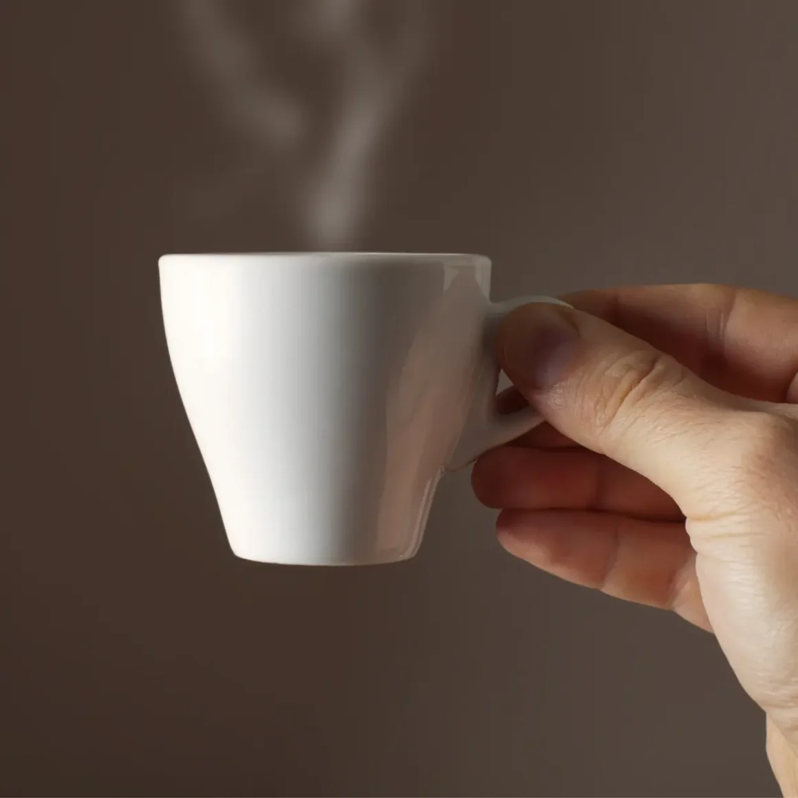 a hand holding a white cup with steam coming out of it