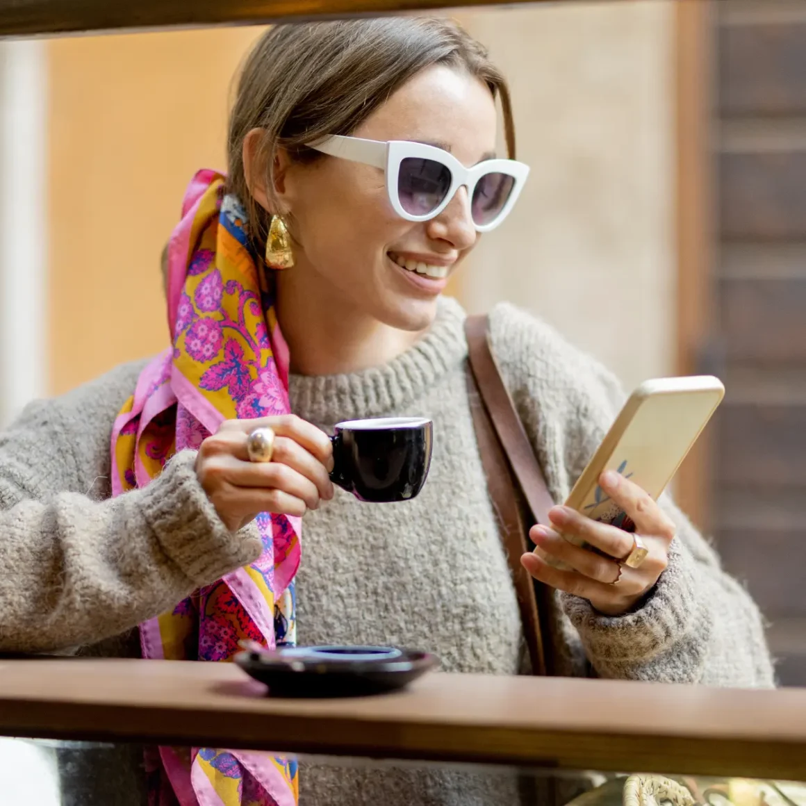 a woman holding a blonde espresso cup and looking at her phone