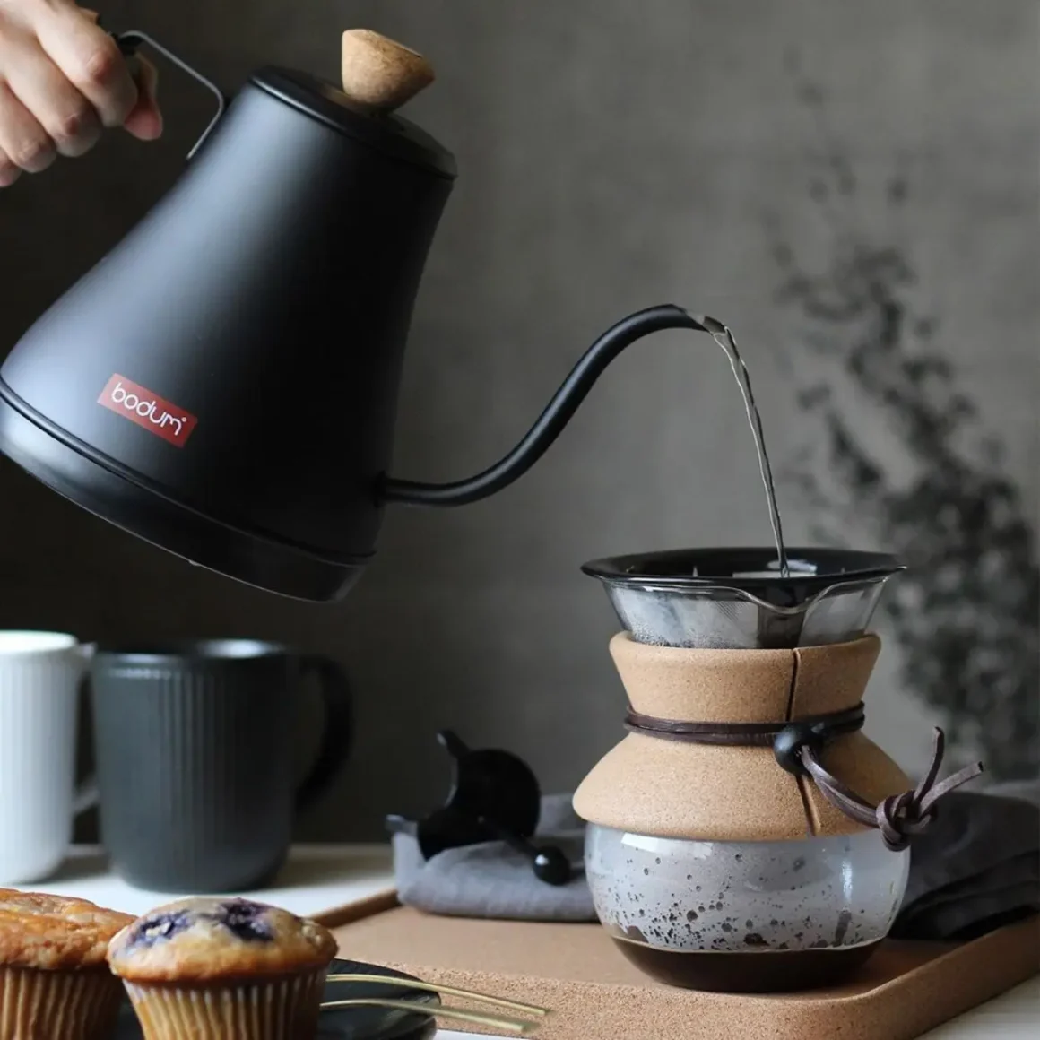 a hand pouring water into a glass coffee maker