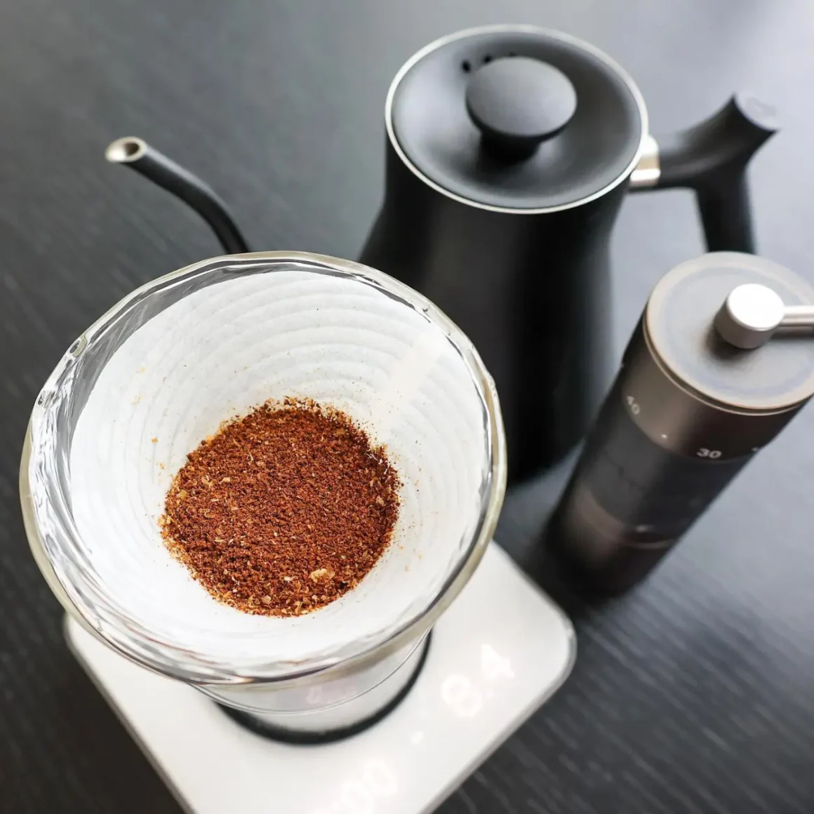 a glass cup with ground coffee in it next to a coffee pot