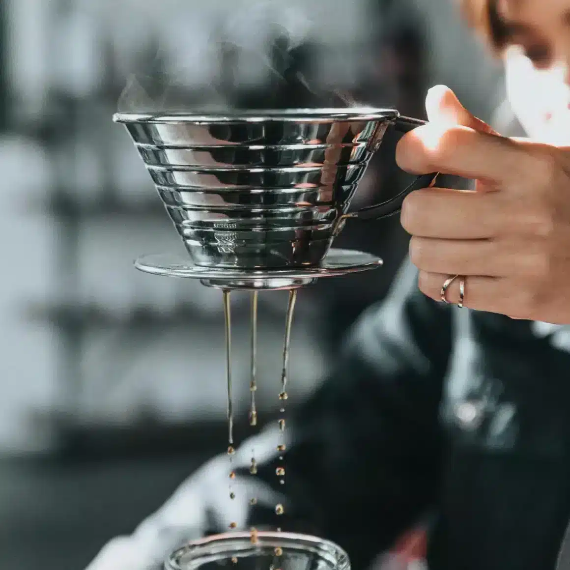 a person holding a metal funnel of kalita wave pour-over coffee maker