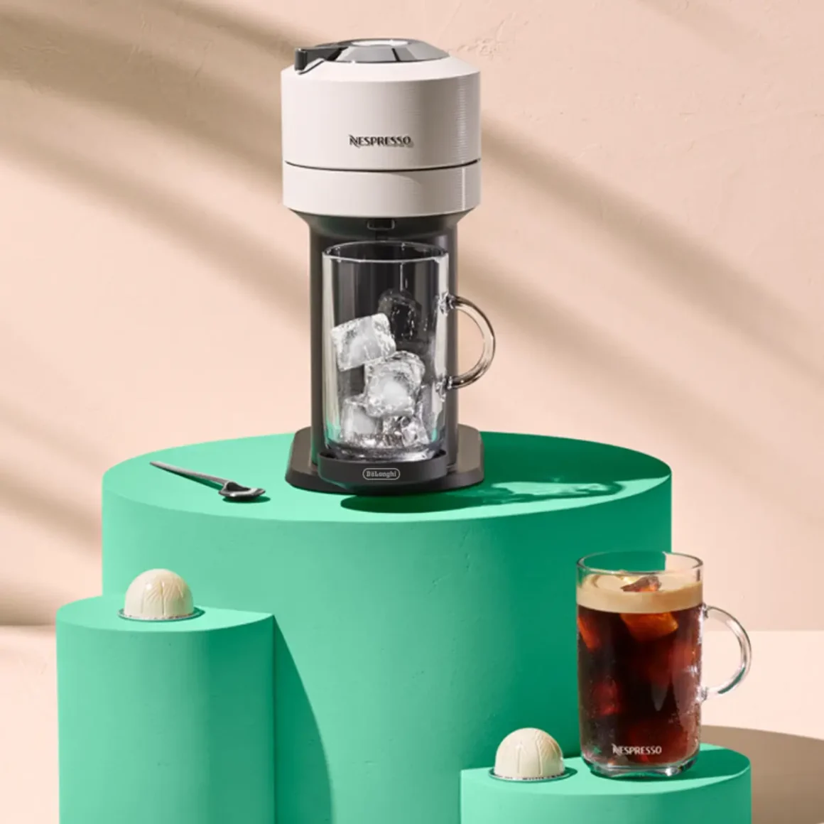 a nespresso vertuo next coffee machine and a glass of coffee on a green pedestal