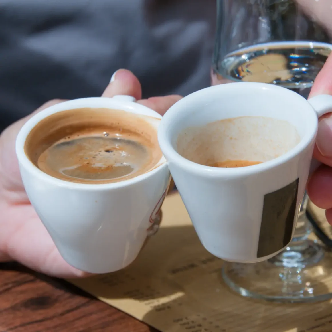 two hands holding cups of blonde espresso