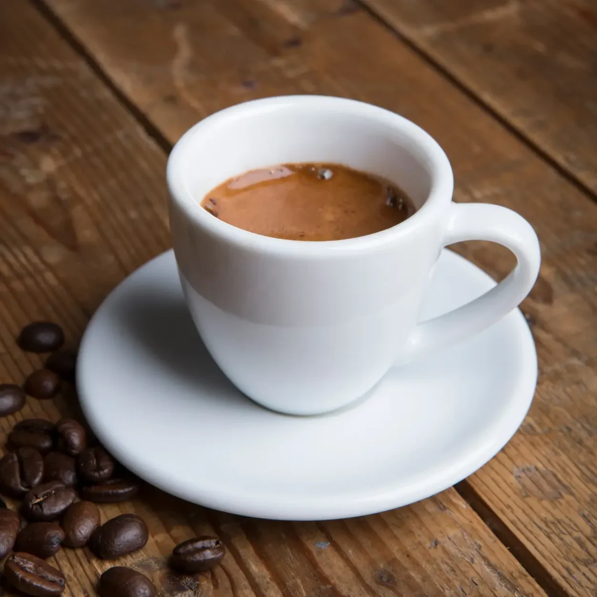 a cup of espresso on a saucer and beans on a wooden surface