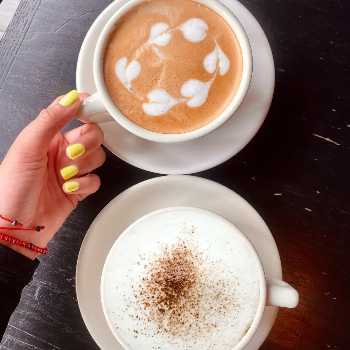 a hand holding a cup of cafe con leche and a cup of latte