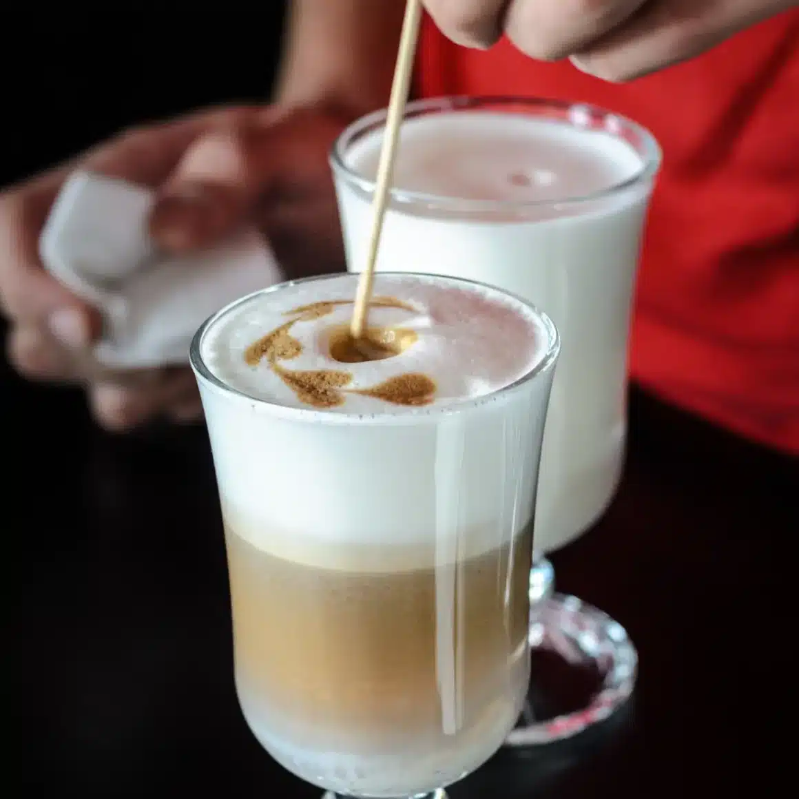 barista creating artistic design on the top of a glass of macchiato coffee
