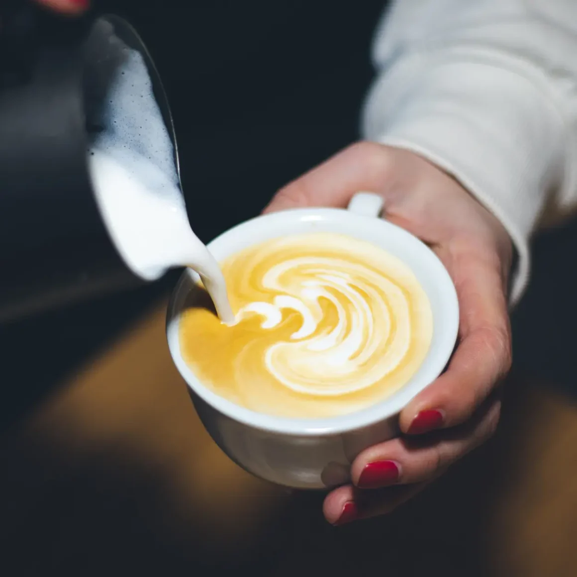 barista making design by pouring milk into a cup of coffee