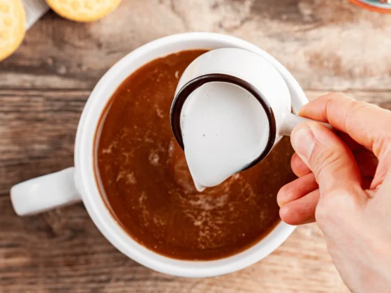 a person pouring coffee creamer into a cup of coffee