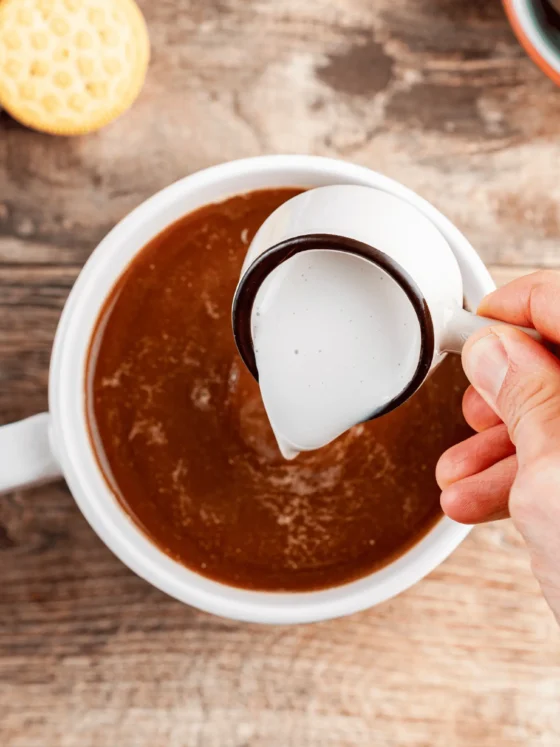 a person pouring coffee creamer into a cup of coffee