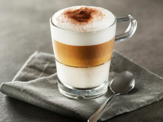 a glass cup with a layered macchiato coffee and a spoon