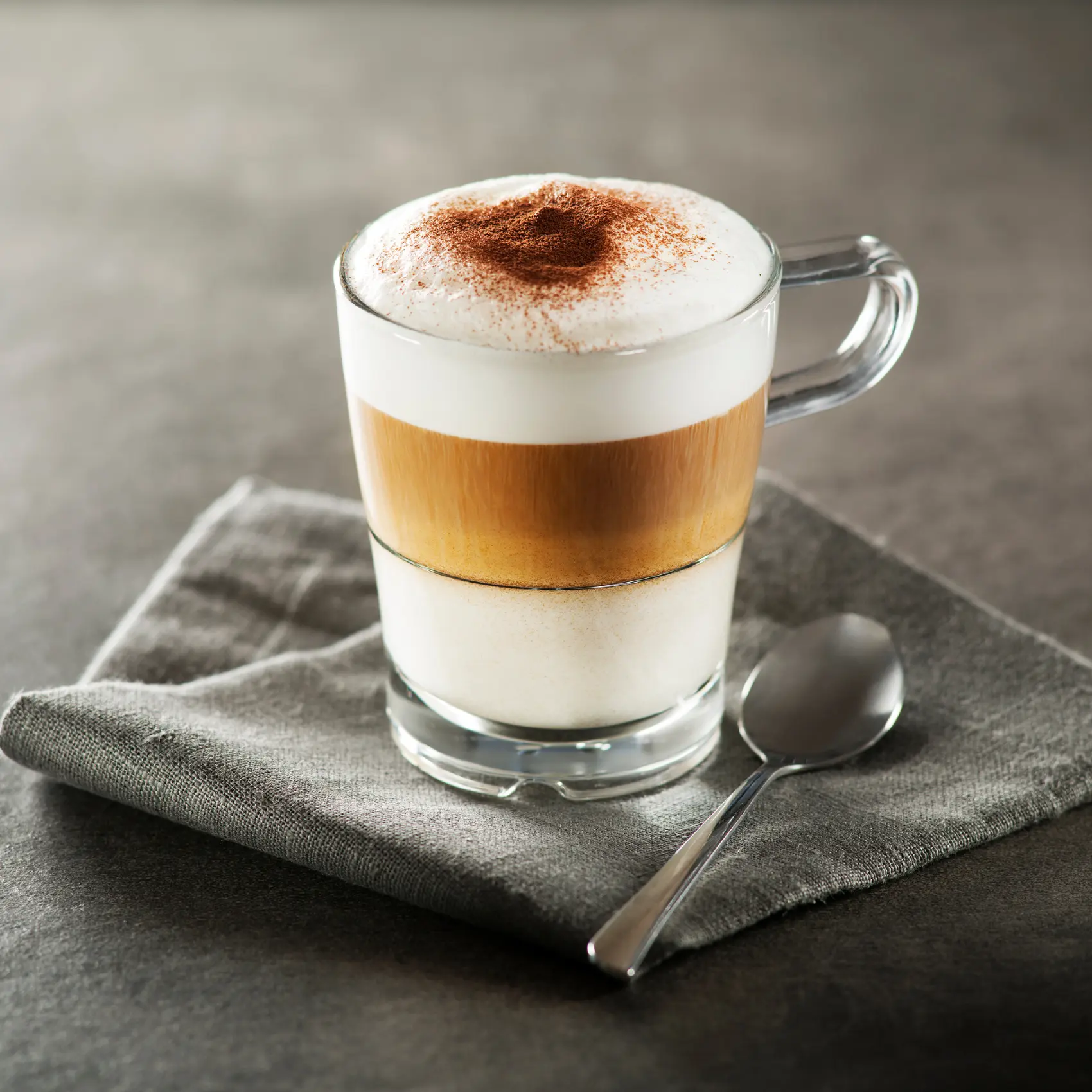 a glass cup with a layered macchiato coffee and a spoon
