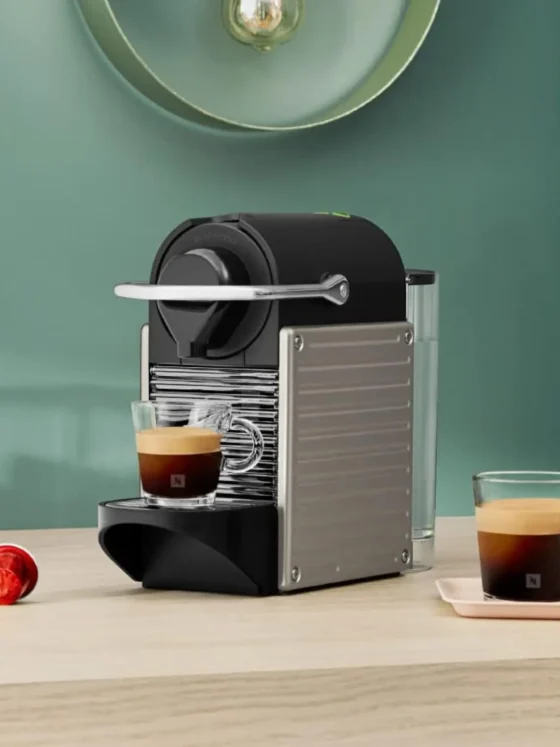 a nespresso pixie espresso machine on a table with two cups of coffee
