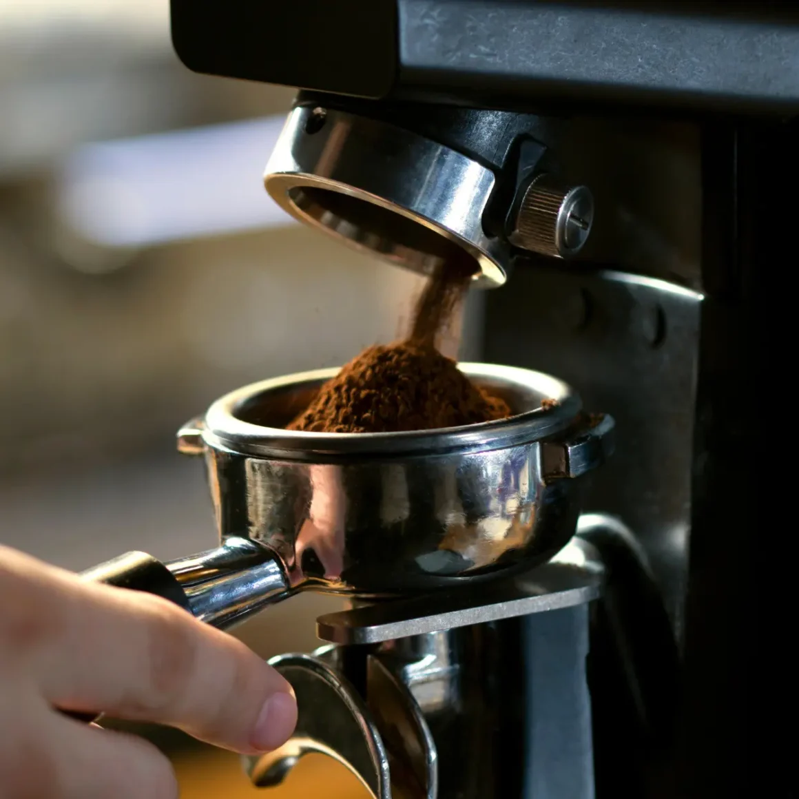 a hand holding a portafilter filled with ground coffee