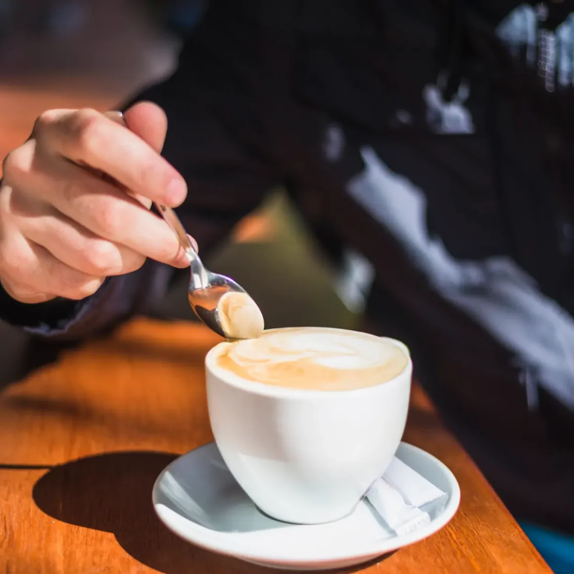 a hand holding a spoon over a cup of latte
