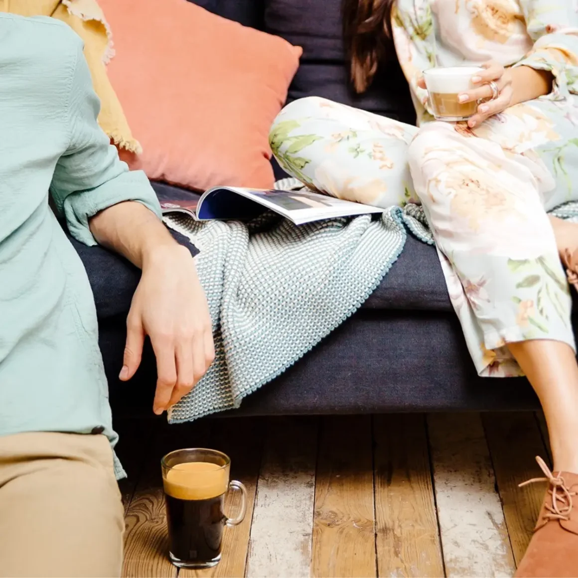 two person sitting on a couch drinking coffee