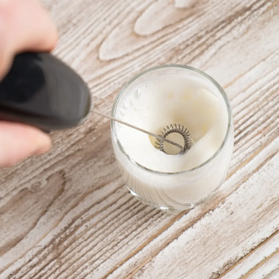 a hand holding a milk frother in a glass with coffee creamer