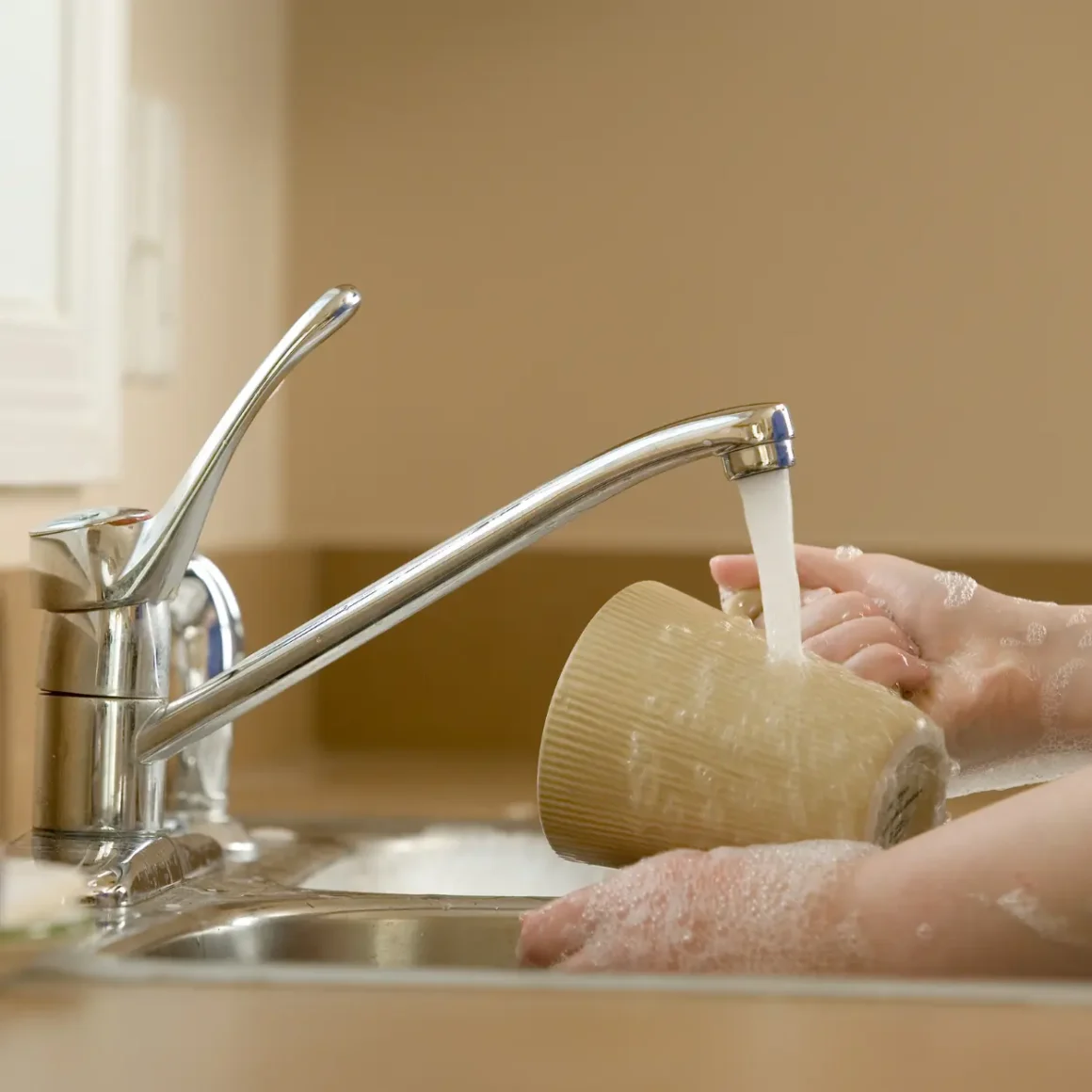 a person washing a ceramic mug in a sink