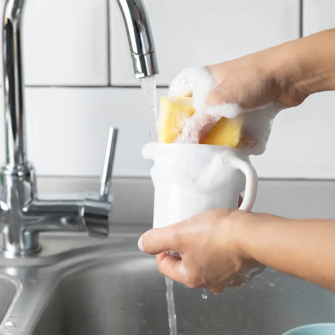 a person washing a porcelain mug with sponge in a sink