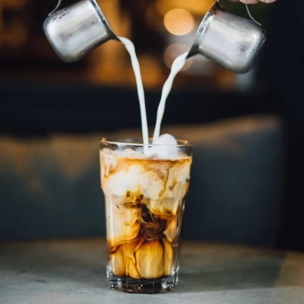 a person pouring milk into a glass of cold latte
