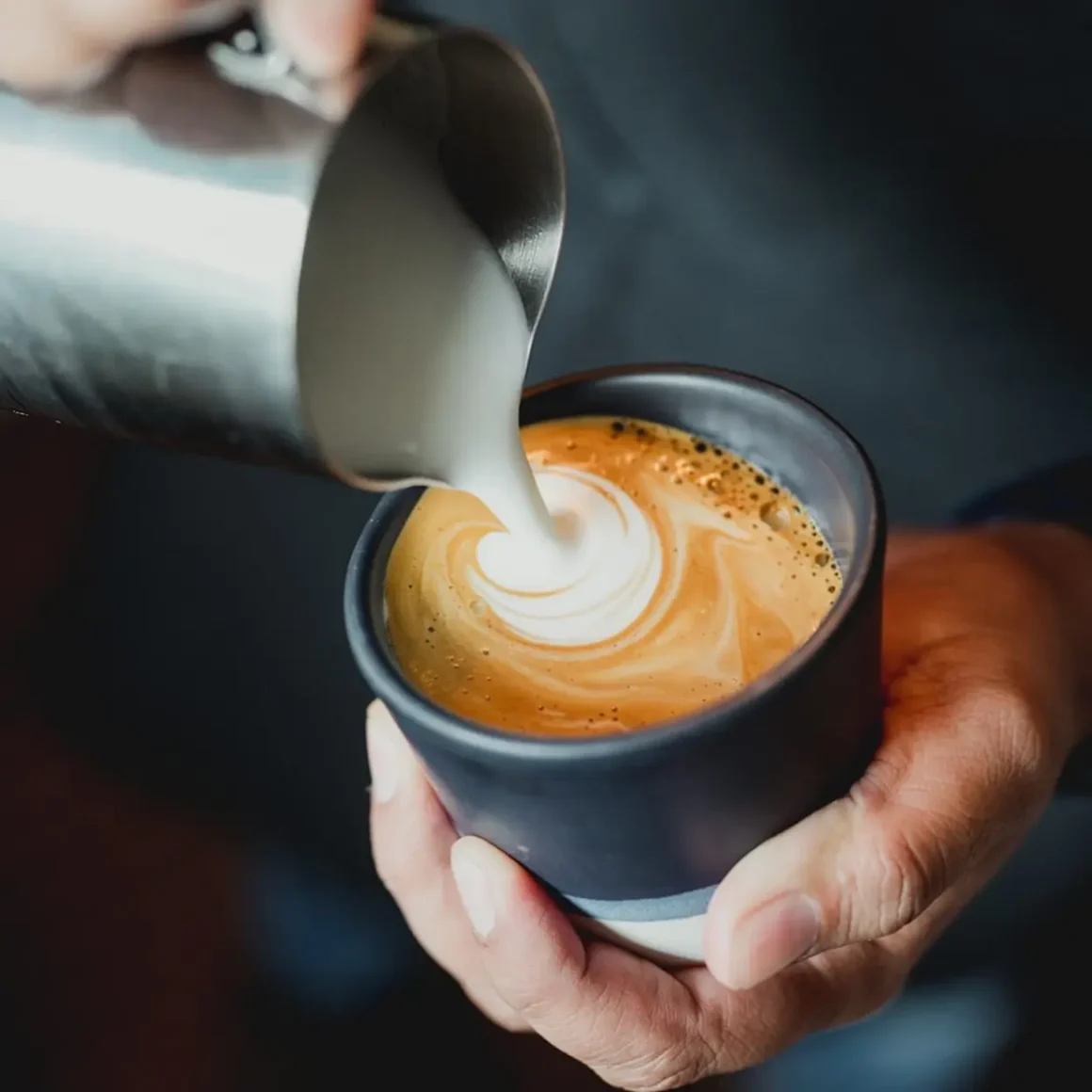 barista pouring milk into a cup of latte