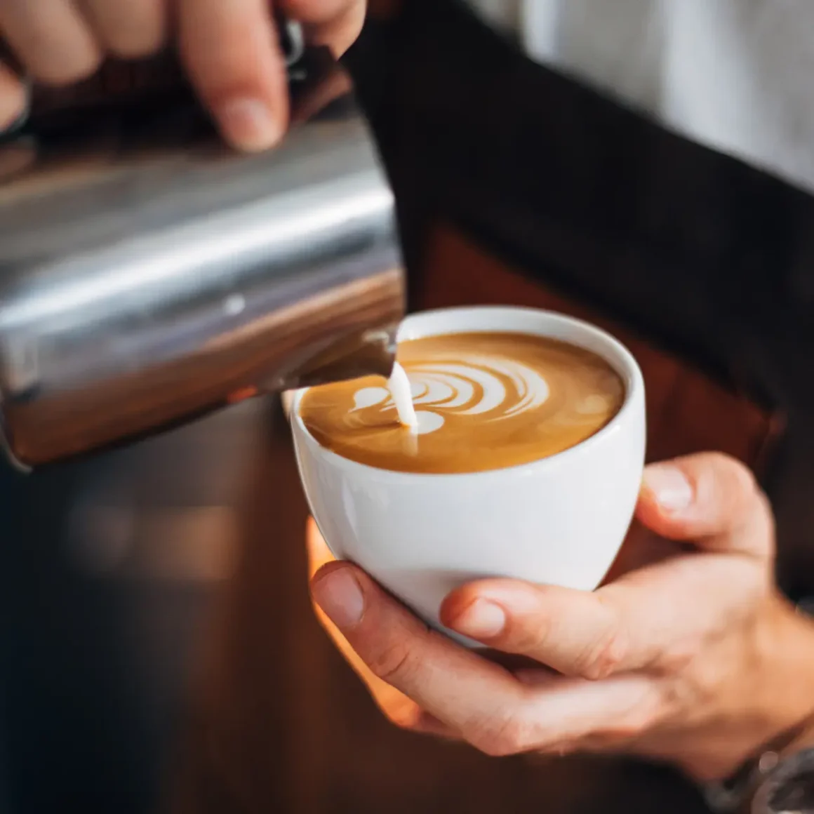 barista pouring milk into a cup of latte
